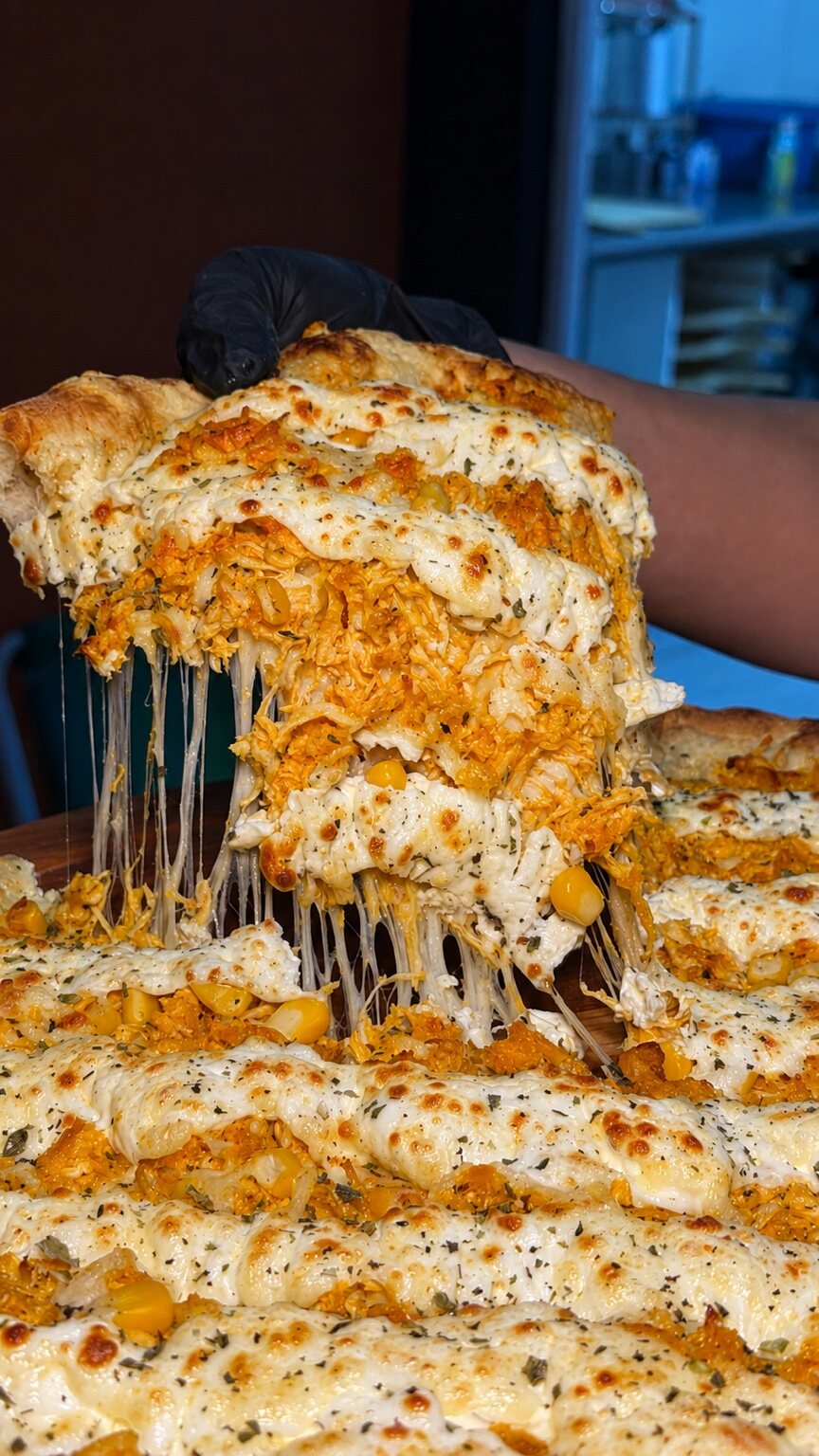 Fatia de pizza cremosa da Luigi’s sendo levantada, com queijo puxando
